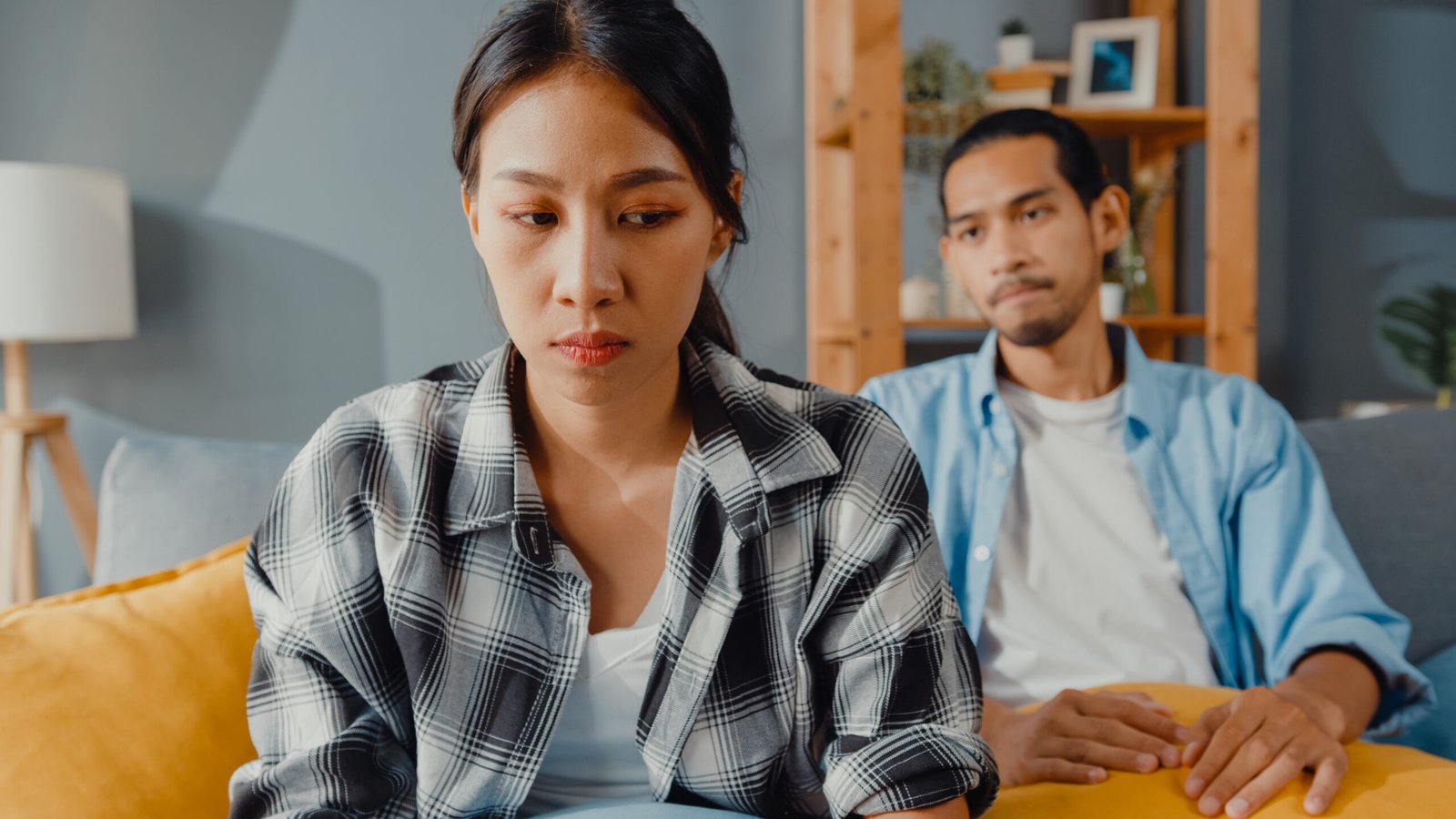 Upset asian couple wife sit on couch listen to furious husband y
